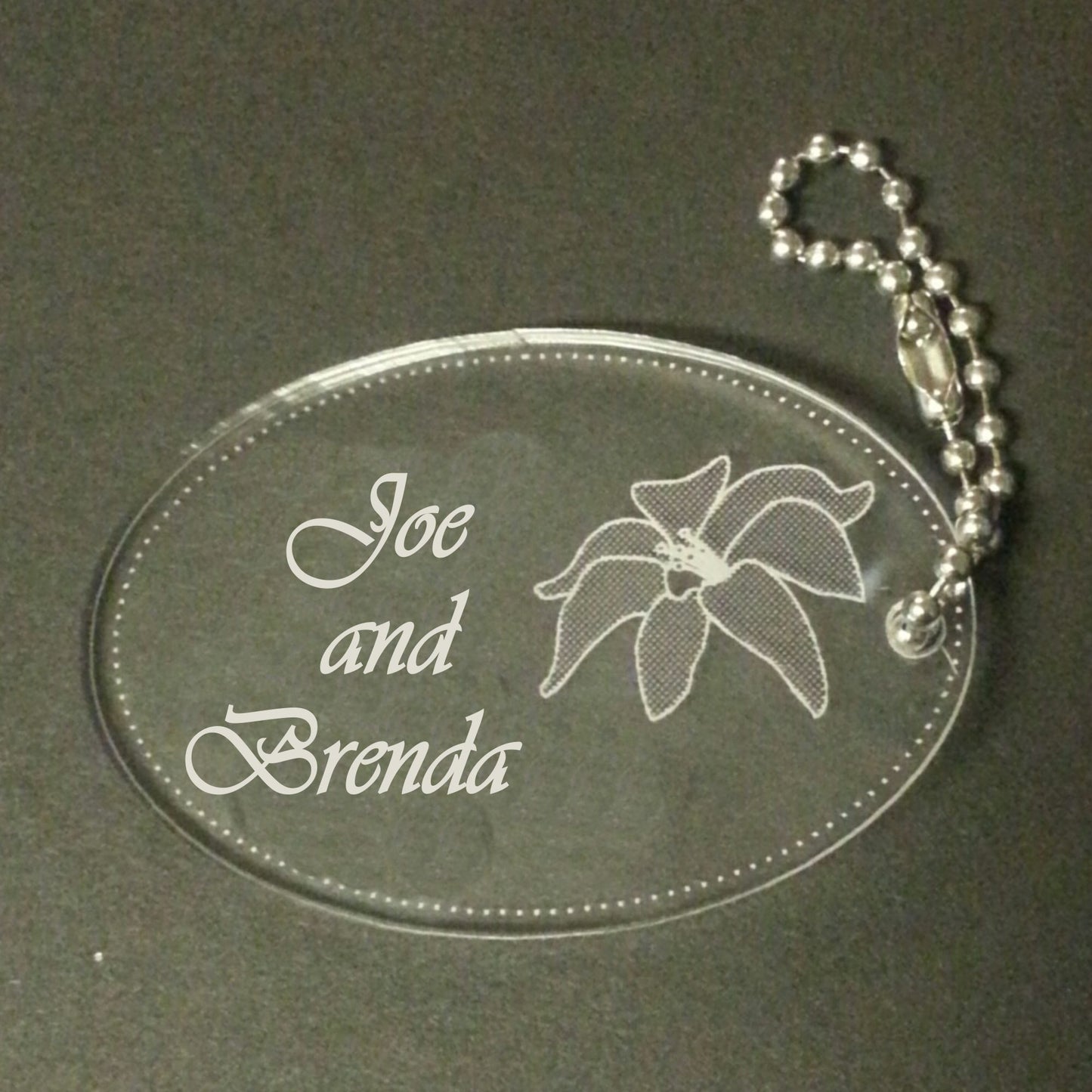 acrylic oval keychain favor engraved with a lily design and attached to a small chain