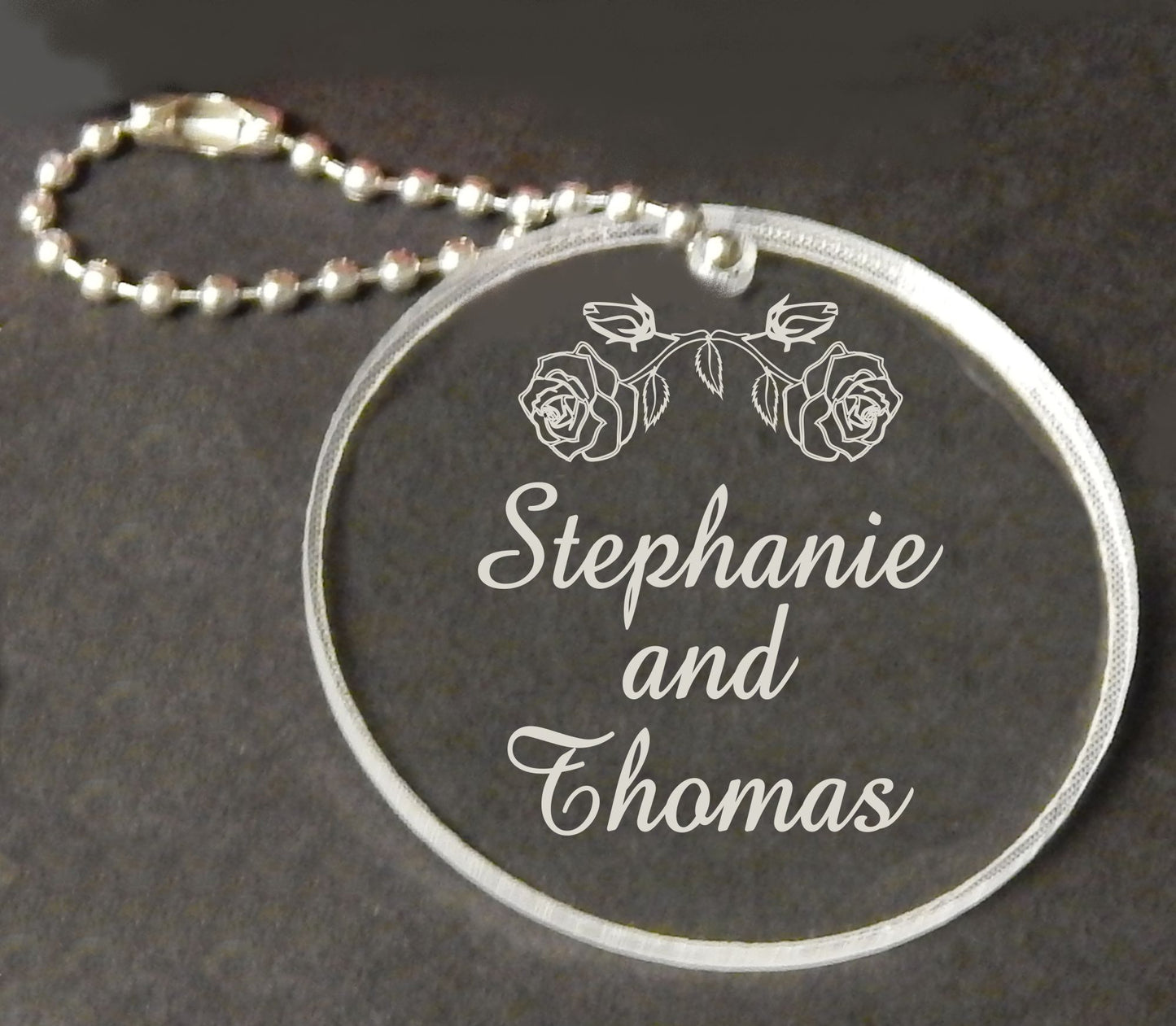 acrylic round keychain favor engraved with a rose design and attached to a small chain