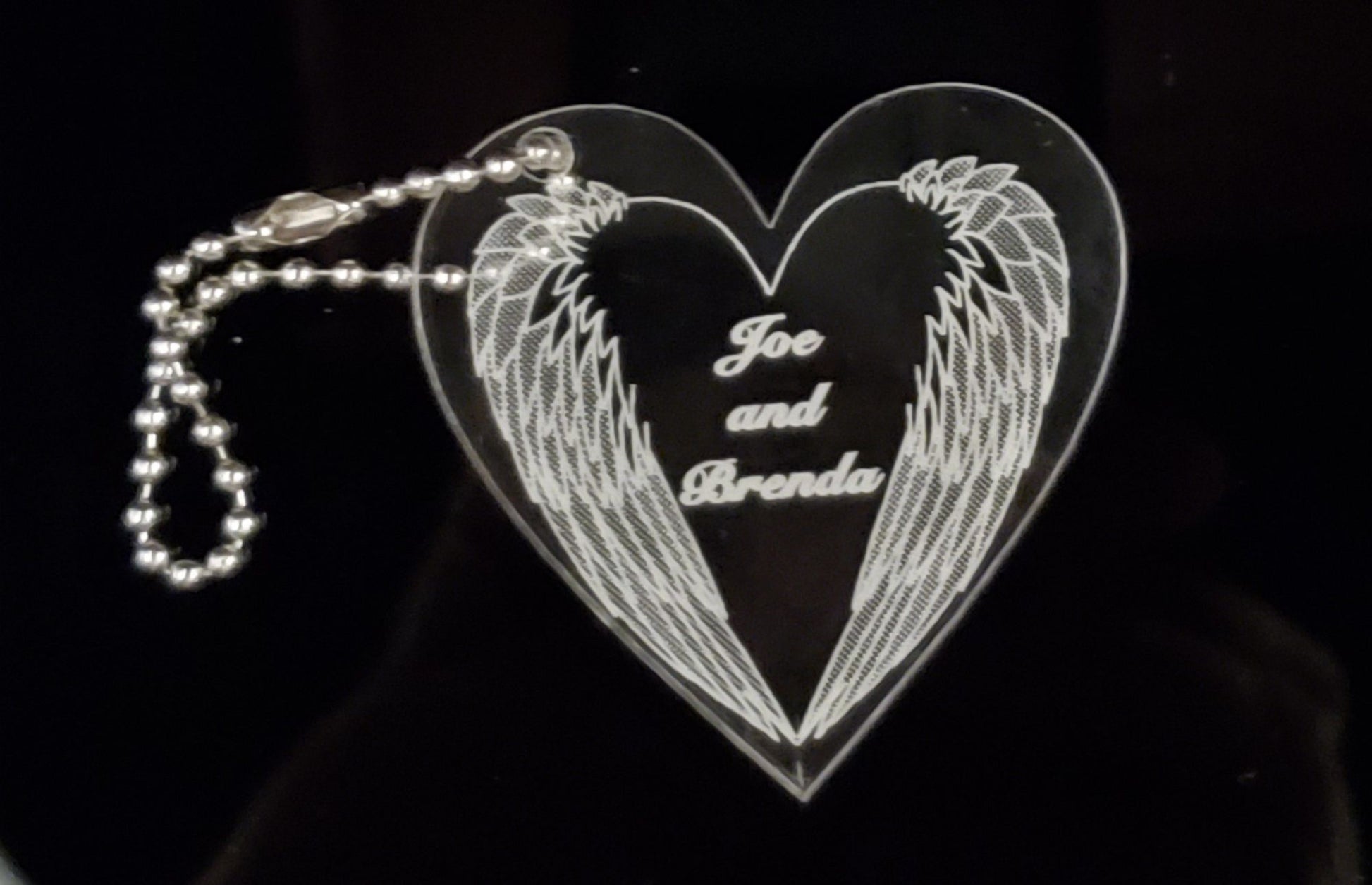 heart shaped acrylic keychain designed with downward angel wings and engraved with names, attached is a small metal chain