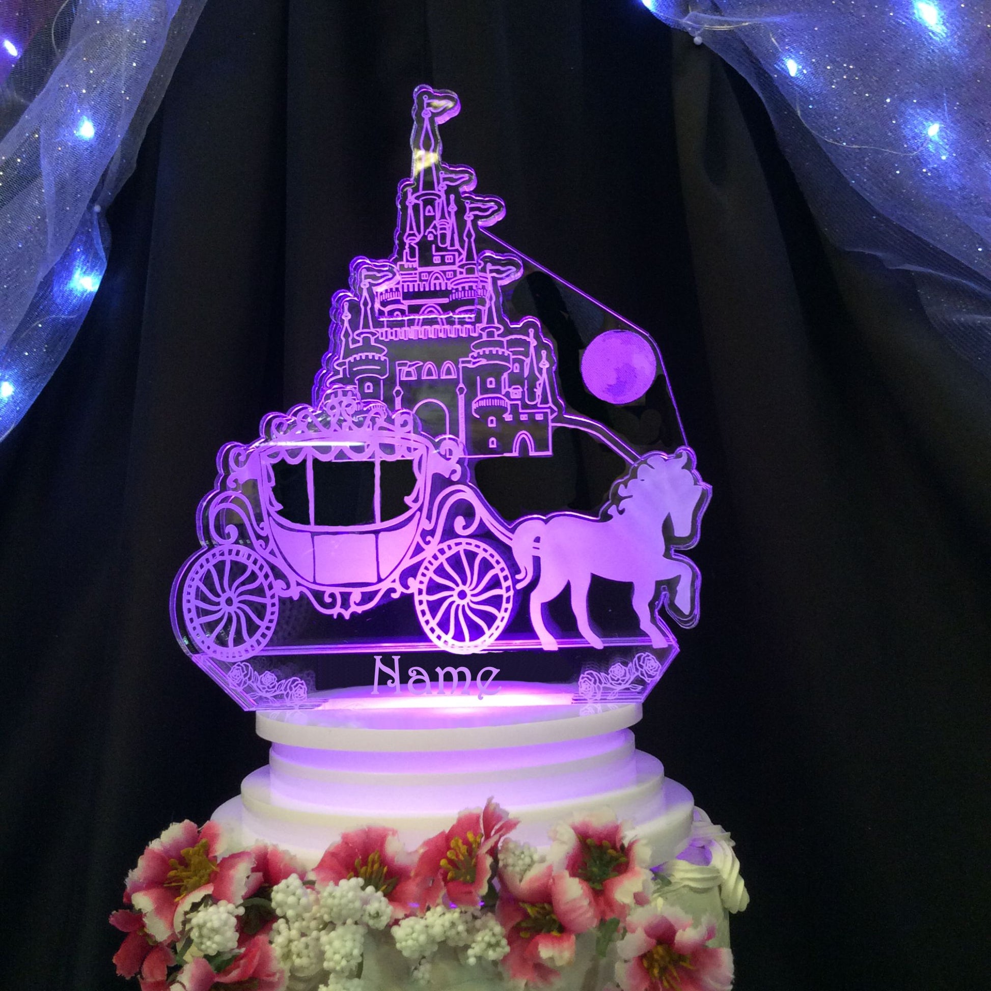acrylic castle and carriage cake topper, shown lit up in a light lavender color, engraved with a name