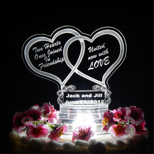 clear acrylic cake topper with a double heart design, with Two Hearts Once Joined In Friendship engraved in one heart and Unite Now with Love engraved in the other, there is also names and date engraved in bottom section of topper