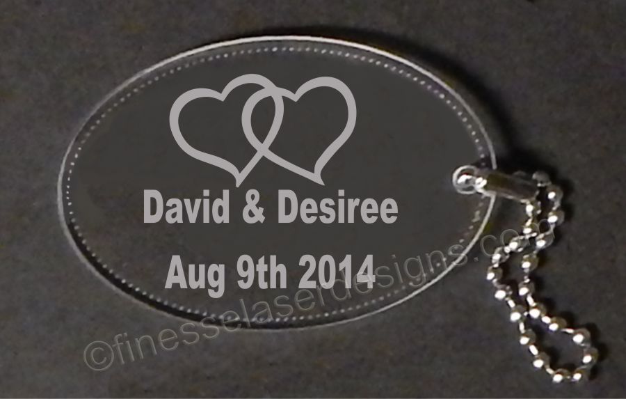 clear oval acrylic keychain engraved with a double heart design along with names and date, a small chain attached