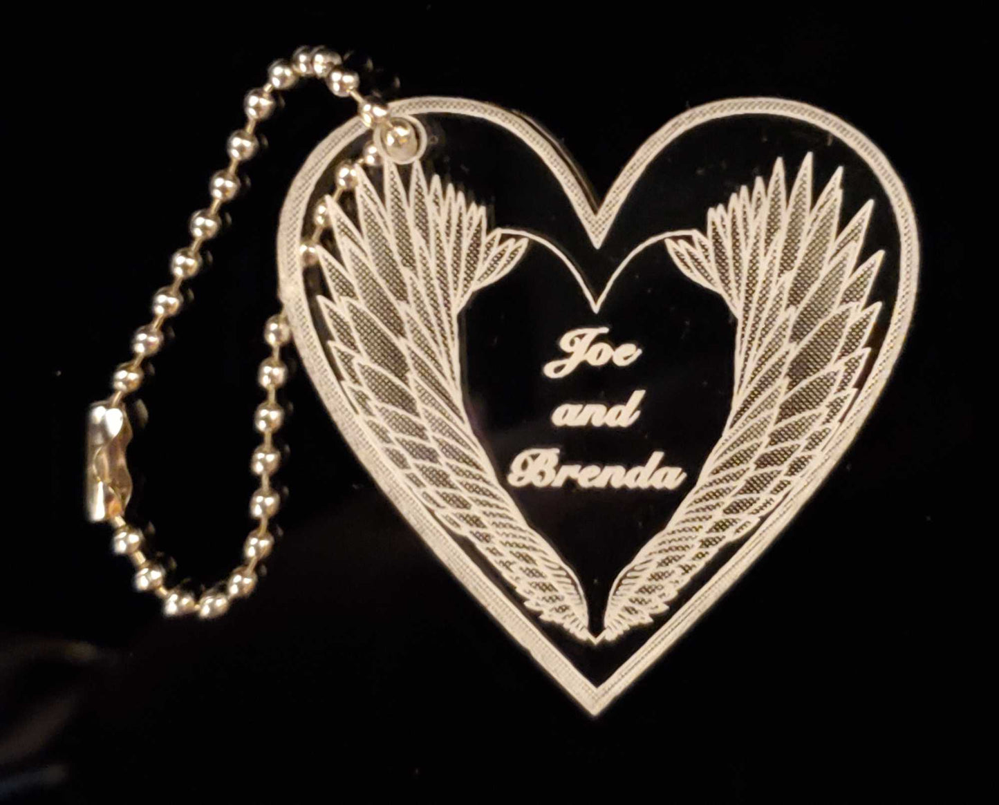 heart shaped acrylic keychain in heart shape with angel wing design engraved with names and a small chain attached