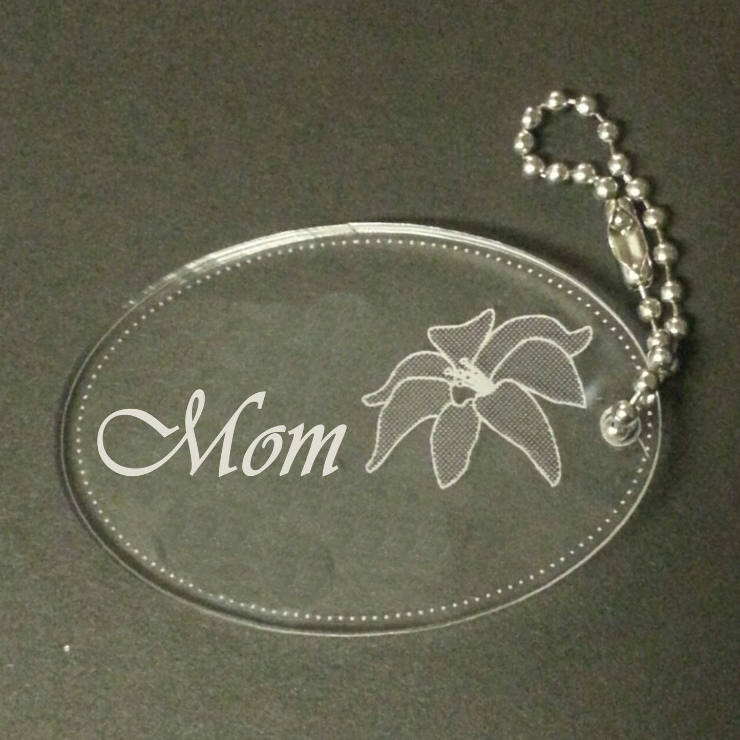 acrylic oval keychain favor engraved with a lily design and attached to a small chain