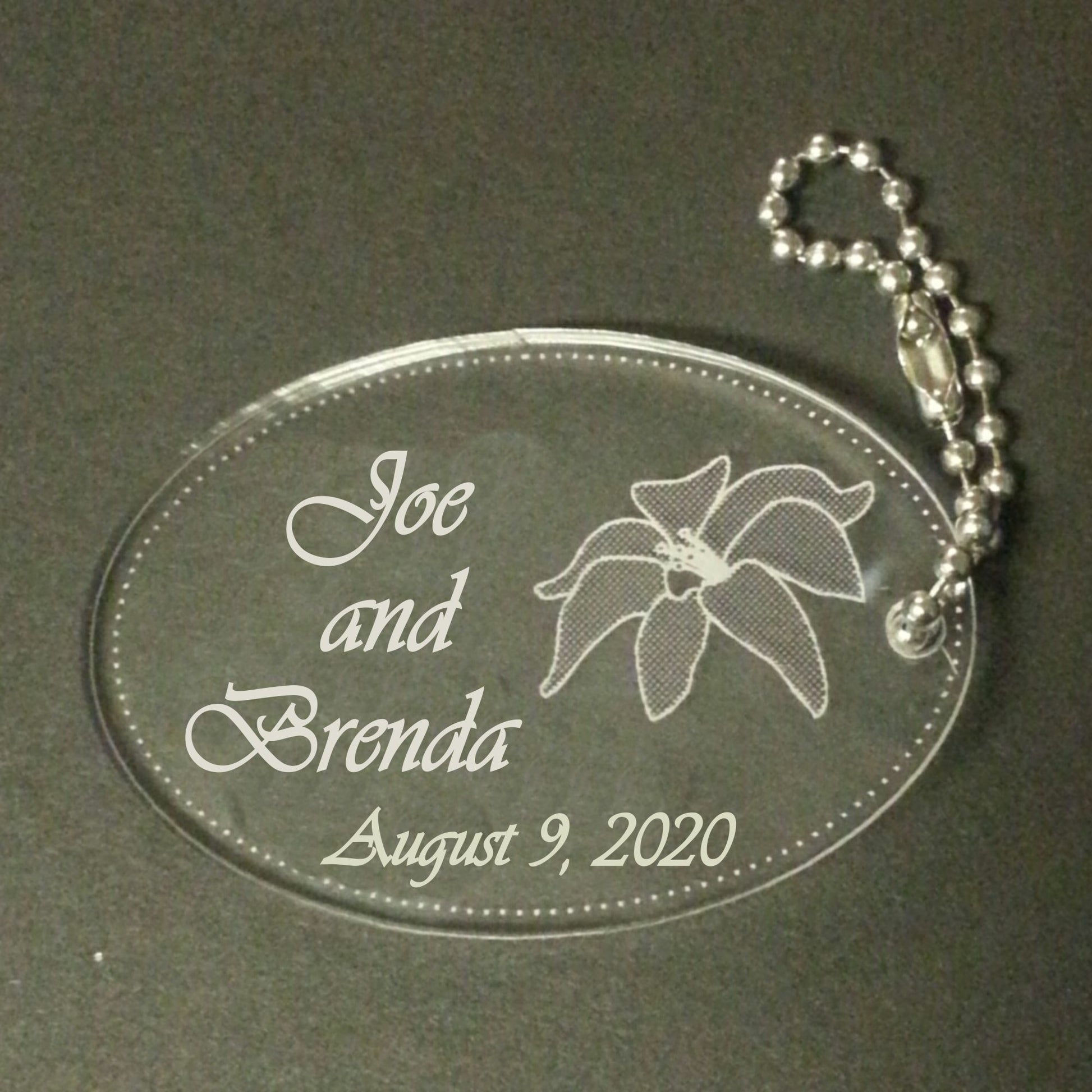acrylic oval keychain favor engraved with a lily design and attached to a small chain