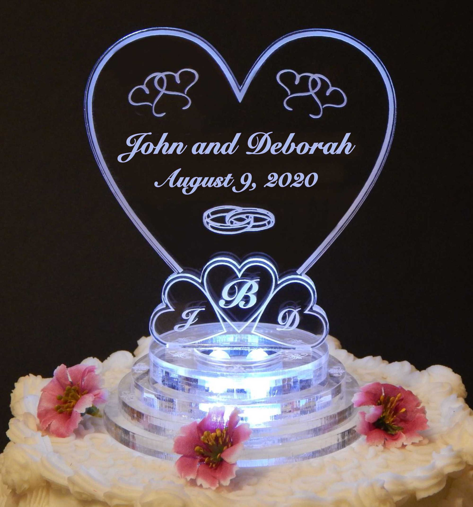 clear acrylic heart shaped cake topper engraved with names, date and 3 monogram letters at bottom inside 3 hearts