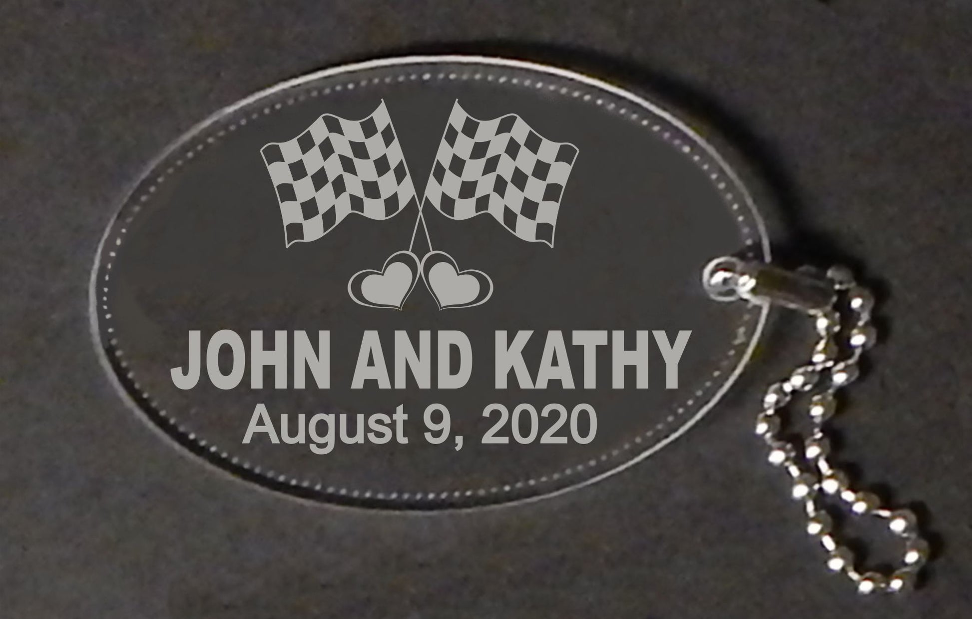 acrylic oval keychain decorated with a set of racing flags and engraved with names and date, with an attached metal chain