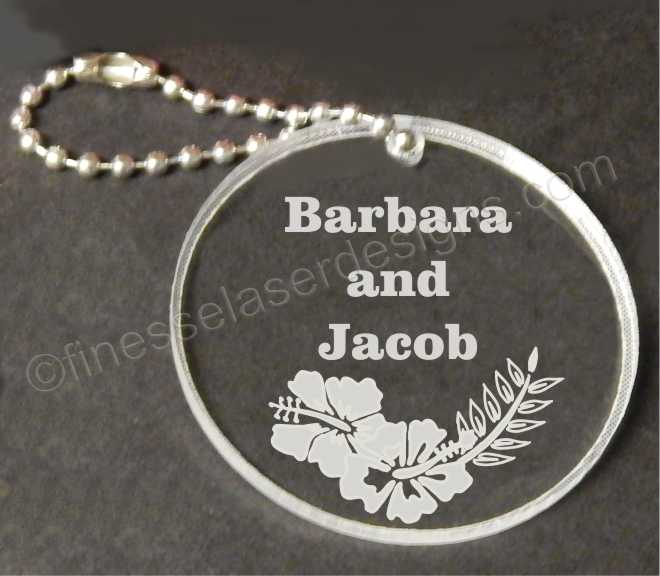 clear acrylic round keychain with hibiscus flower design and engraved with names along with a small chain attached