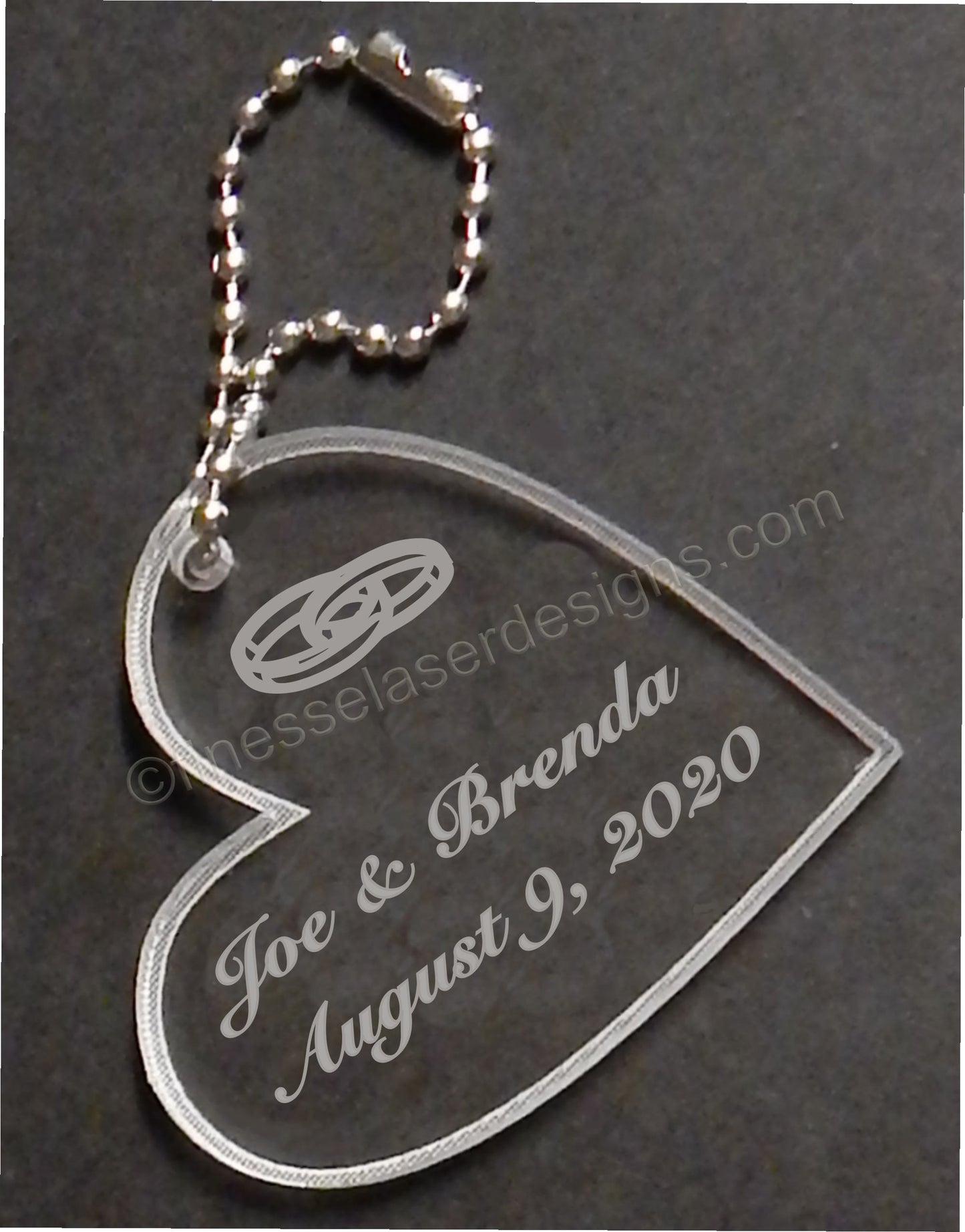 heart shaped acrylic keychain engraved with names and date and a wedding ring design, with a small metal chain attached
