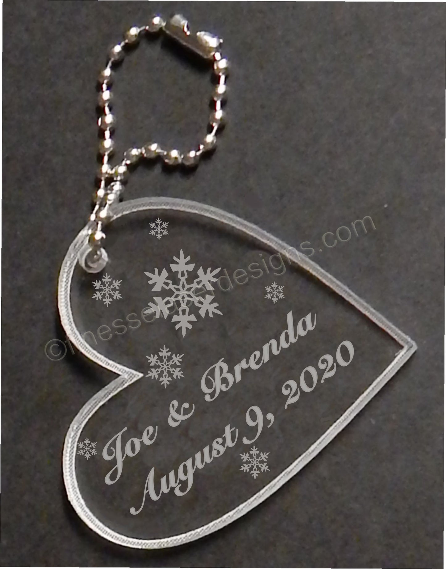 heart shaped acrylic keychain designed with snowflakes and engraved with names and date, with attached small metal chain