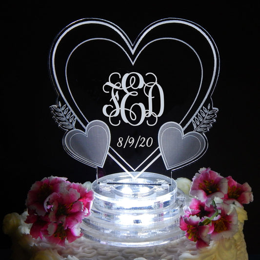 heart shaped acrylic cake topper shown with monogram and date, lit up and sitting on top of a cake decorated with flowers