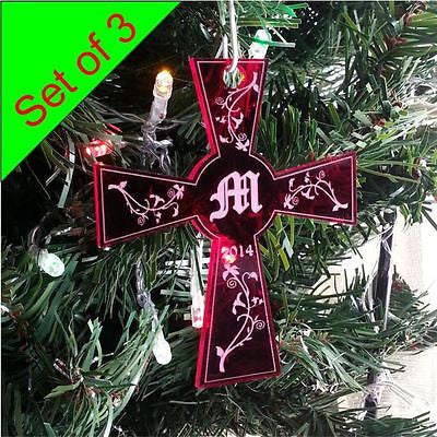 red cross shaped ornament hanging on a tree with single initial engraved in center