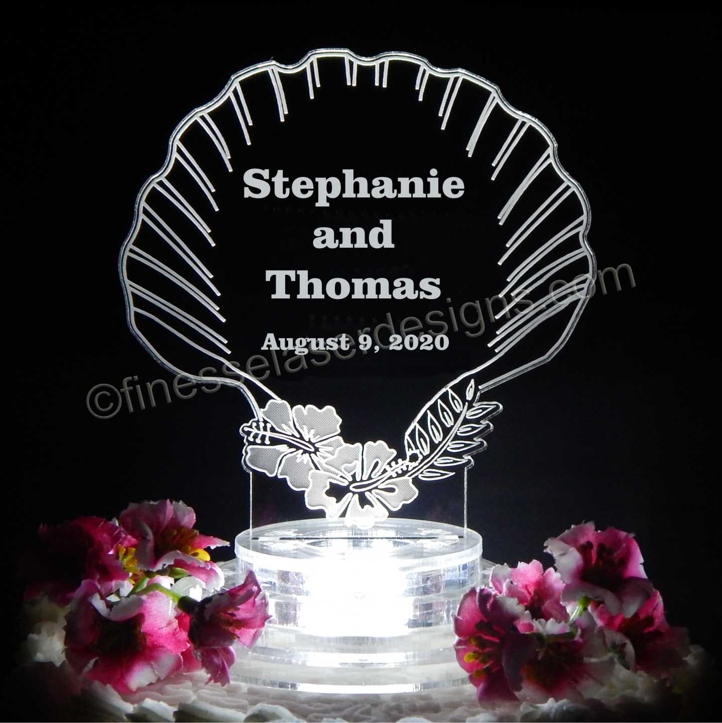 Clear acrylic seashell shaped cake topper lighted up with a white light and engraved with names and date