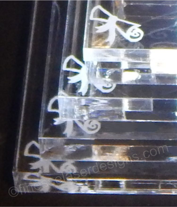 partial view of an acrylic cake topper base showing a graduation scroll design on the corner of each tier