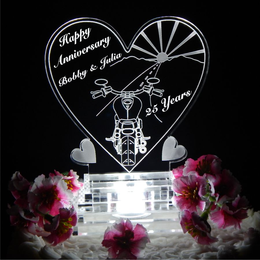 Acrylic heart shaped cake topper with a back view of a motorcycle driving towards a sunset, with Happy Anniversary