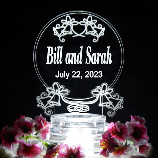 acrylic cake topper decorated with bells and wedding rings along with names and date
