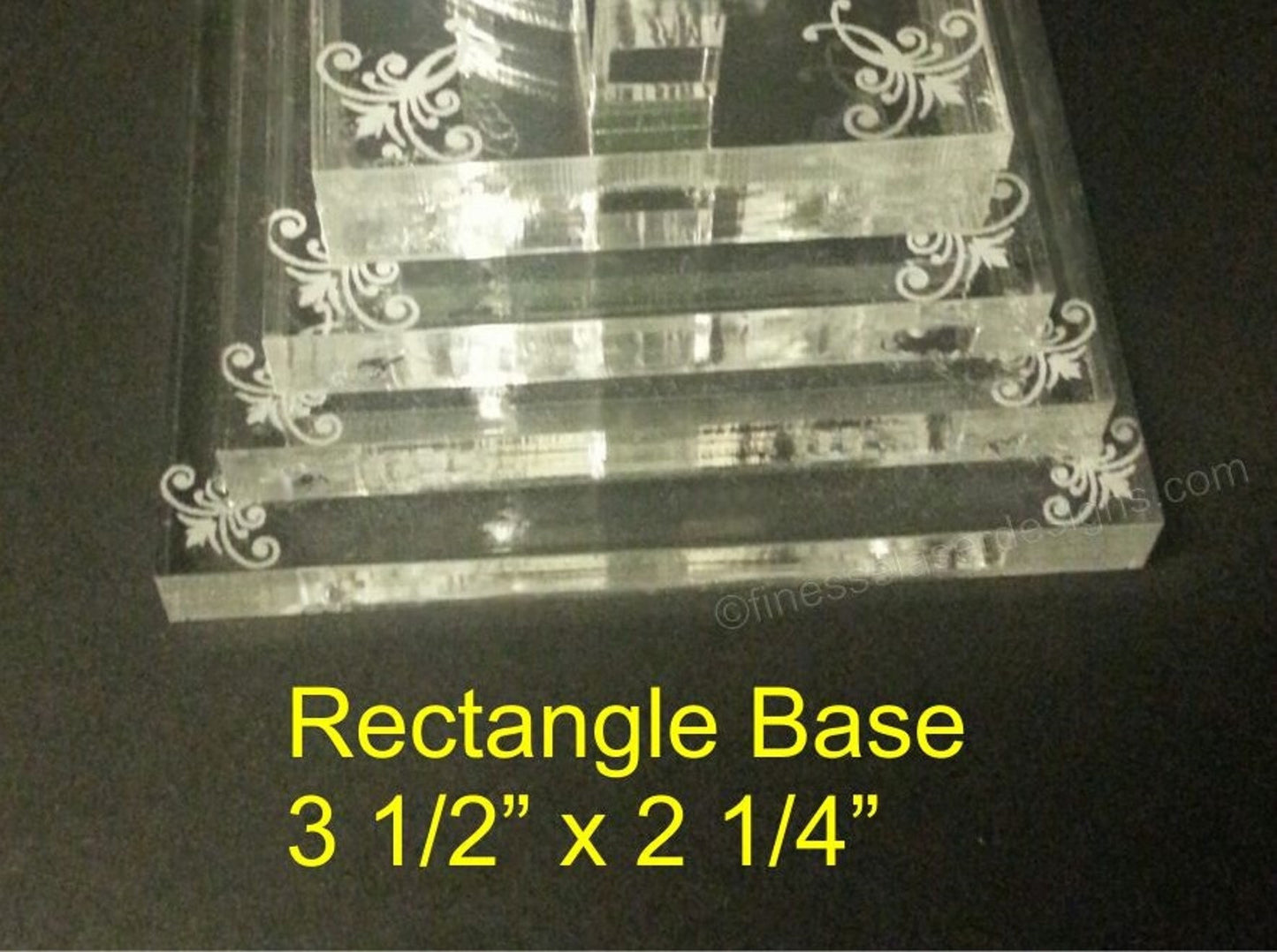 partial picture of an acrylic rectangle tiered base for a cake topper with pretty designs on each layer